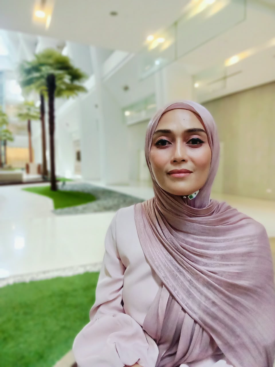 Anne Ardzi wearing a blush pink hijab in a bright indoor garden